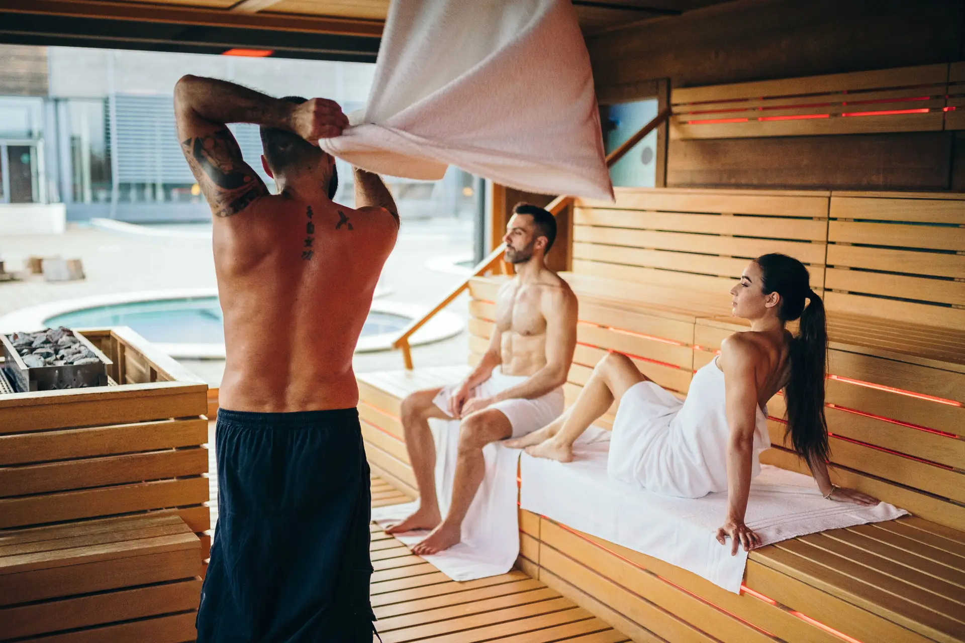 Couple relaxing in the sauna, enjoying a day at the spa. Man arranging a towel.