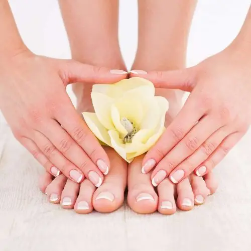 Woman's hands and feet with French manicure, delicate flowers in between.