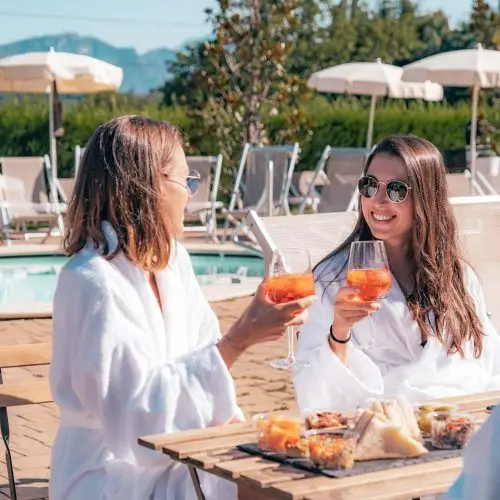 Due donne in accappatoio sorseggiano un aperitivo con cocktail a bordo piscina.