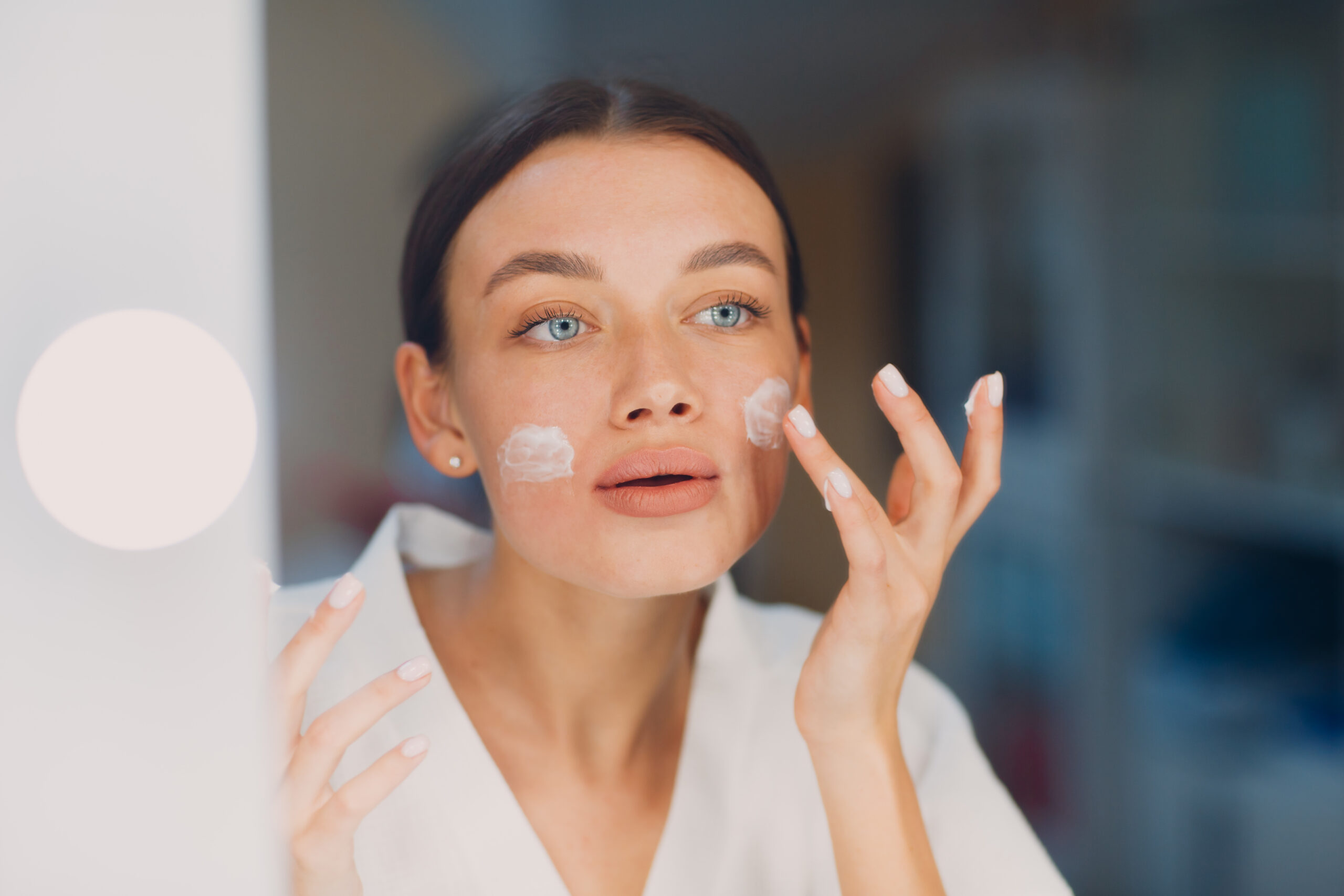 Donna che applica la crema per il viso, routine di cura della pelle.