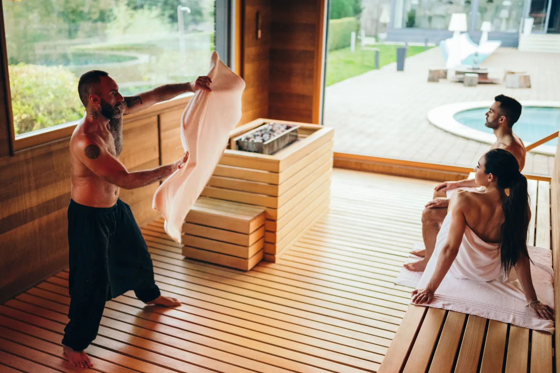 Un uomo in una sauna offre asciugamani a una coppia durante una cerimonia di benessere.