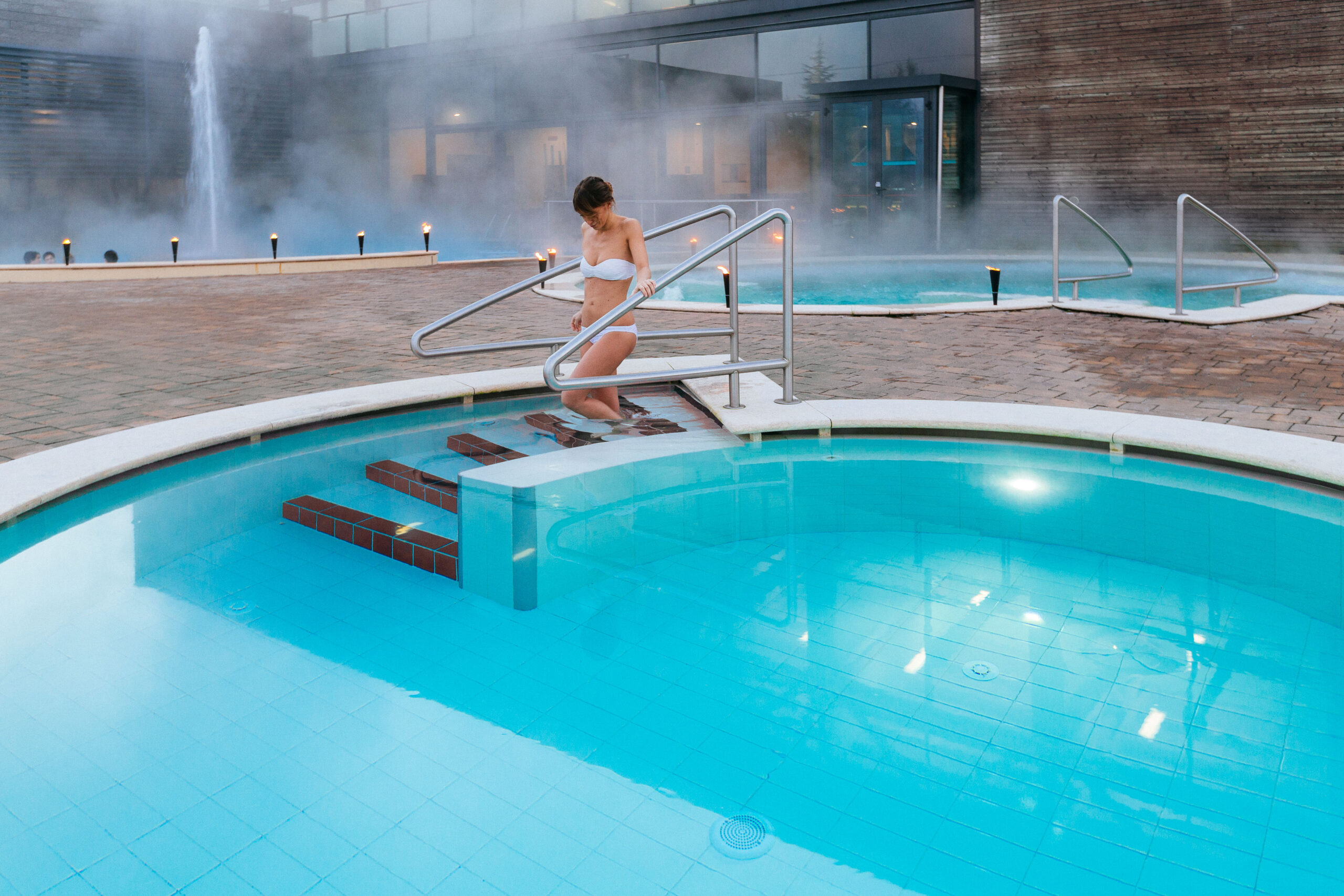 Persona che entra in una piscina termale all'aperto fumante in un centro benessere