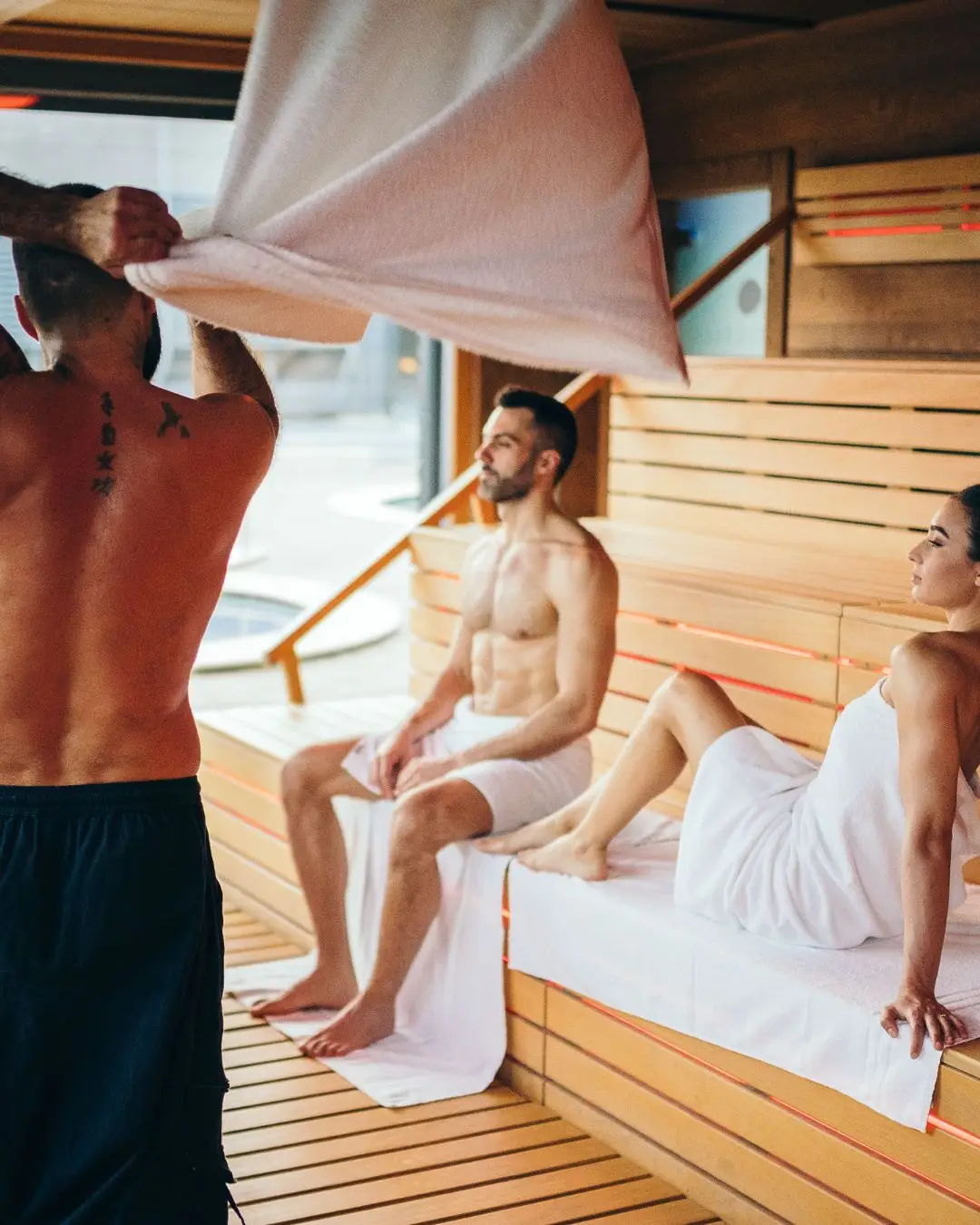 Uomo che esegue l'Aufguss in una sauna con due persone che si rilassano