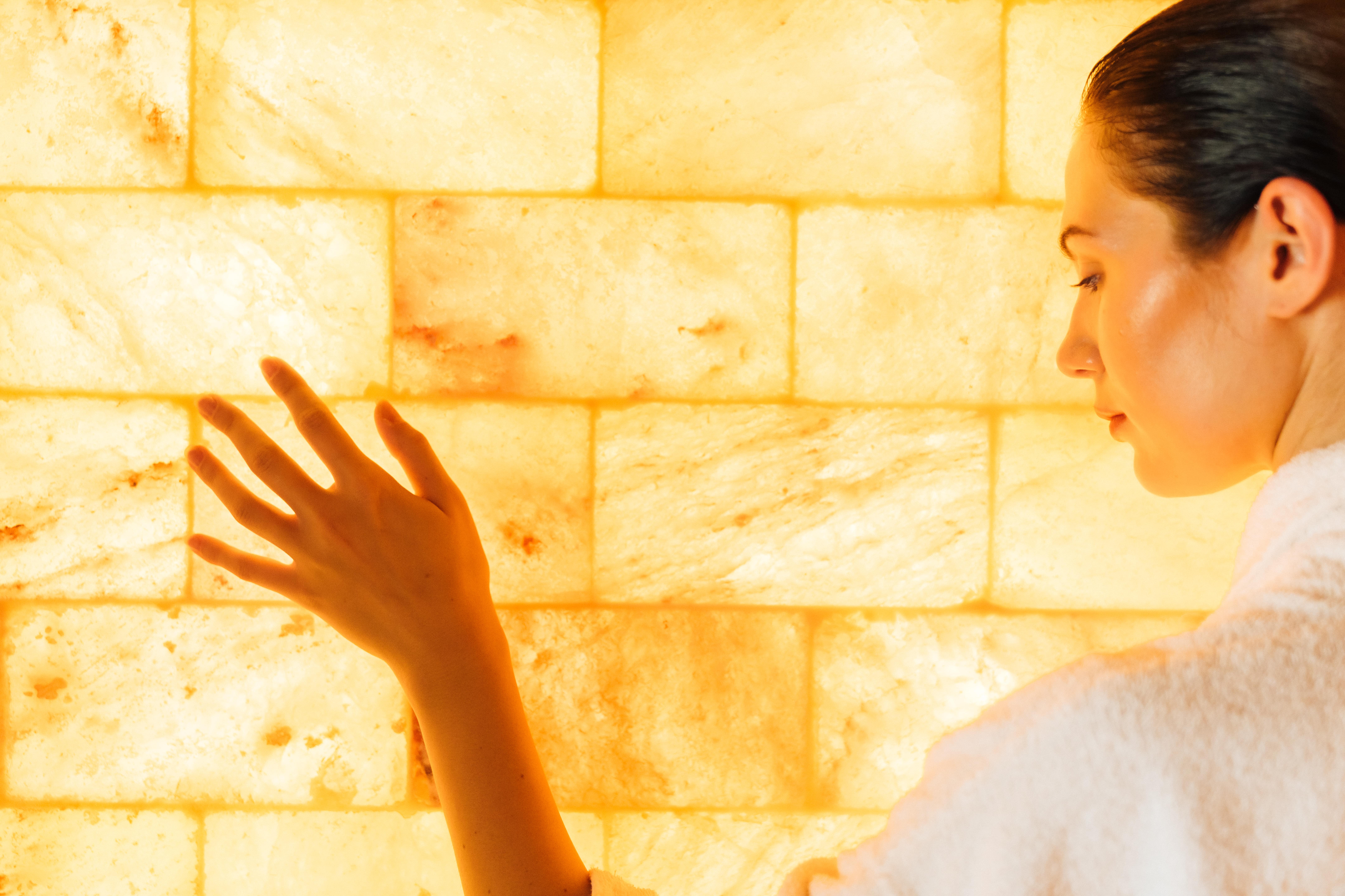 Donna in accappatoio di fronte a parete di sale illuminata. Percorso Benessere