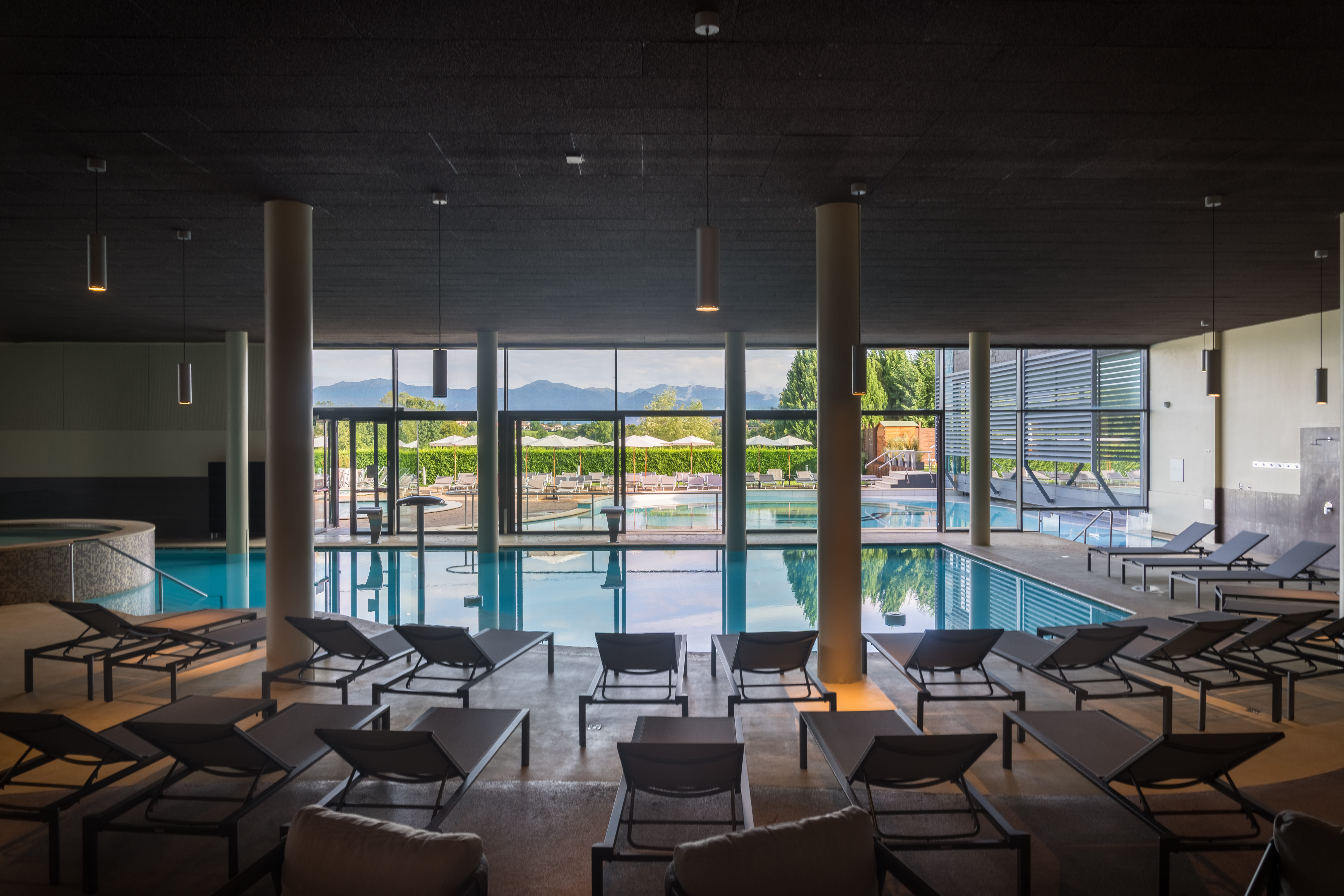 Interno di piscina con lettini e vista esterna, ideale per un percorso benessere.