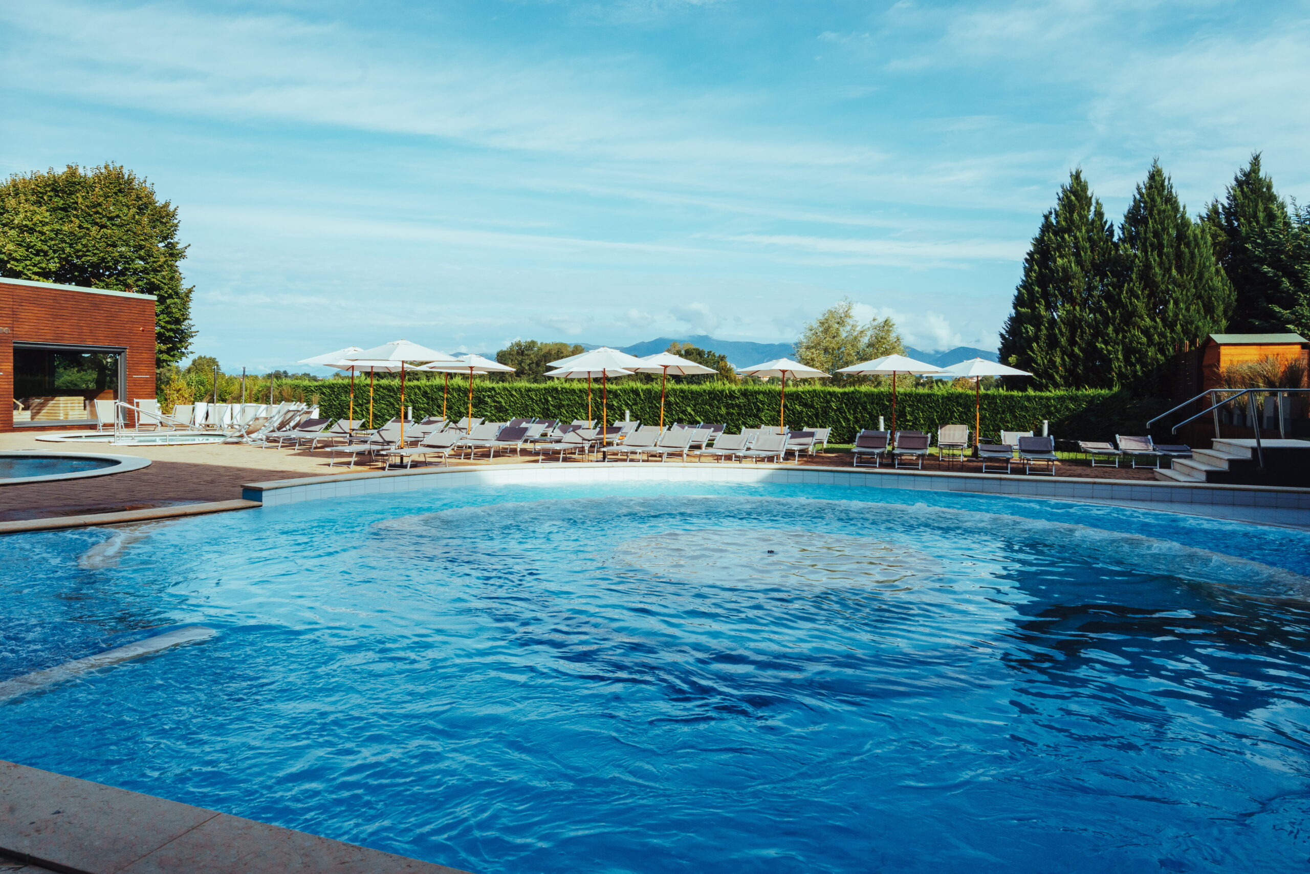 Piscina azzurra con lettini e ombrelloni, ideale per un percorso benessere rilassante.