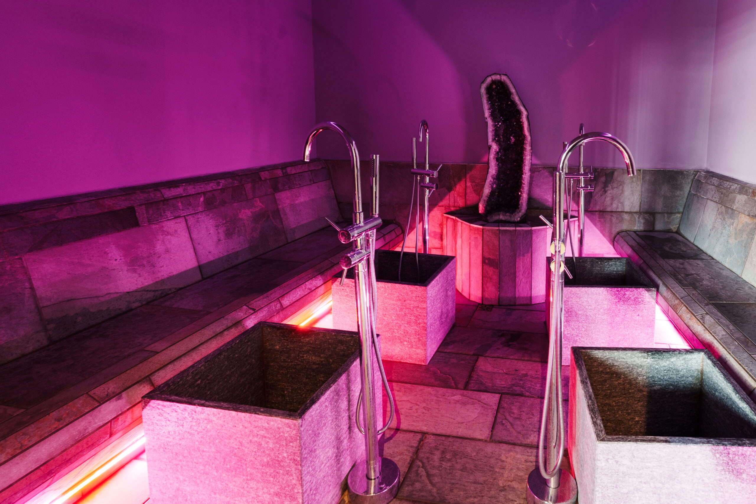 Percorso benessere: vasche per idromassaggio con illuminazione viola e panche in pietra.