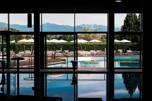 Vista piscina interna con ombrelloni e montagne sullo sfondo.